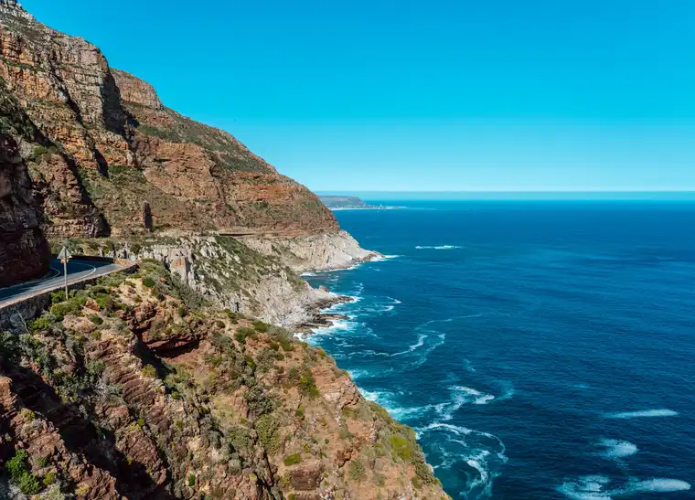Скальная дорога Chapman’s Peak изгибается над синим Атлантическим океаном под ясным дневным небом