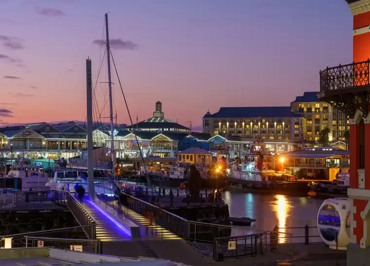Яхты, портовые суда и здания V&A Waterfront в фиолетовом свете после заката